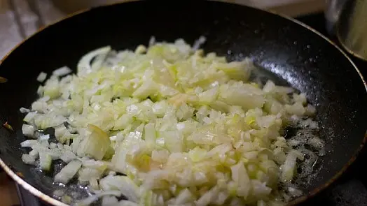Smažené nakrájené cibule v pánvi pro recept na králíka.