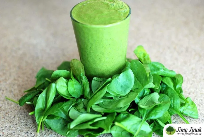 Sklenice zeleného smoothie položená na čerstvém špenátu.