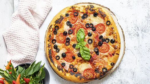 Připravená pizza z kynutého těsta s rajčaty a bazalkou.