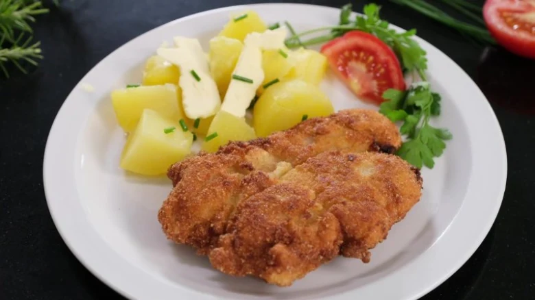 Zlatě opečený řízky s bramborami na bílém talíři.