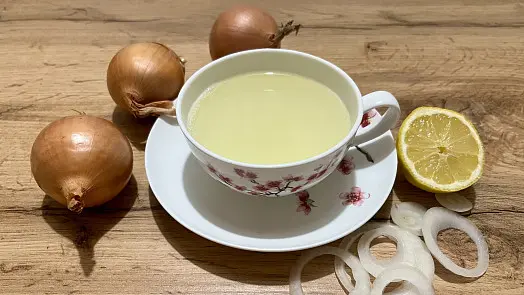 Šál cibulového čaje s citronem a surovou cibulí na dřevěném stole.