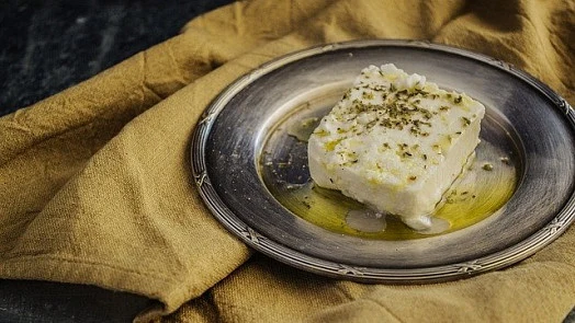 Kousek domácího sýra z mléka a vajec posypaného bylinkami.