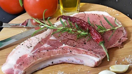 Surová vepřová pečeně s kořením na dřevěném talíři.