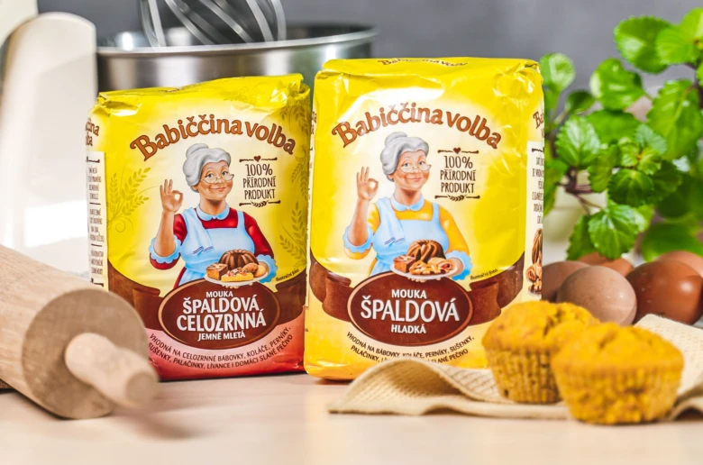 Dvě balení špaldové mouky vedle vajec a muffinů na kuchyňské desce.