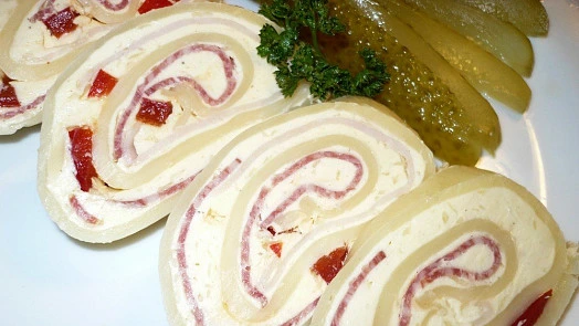 Nakrájené sýrová roládka se šunkou a okurkou na talíři.