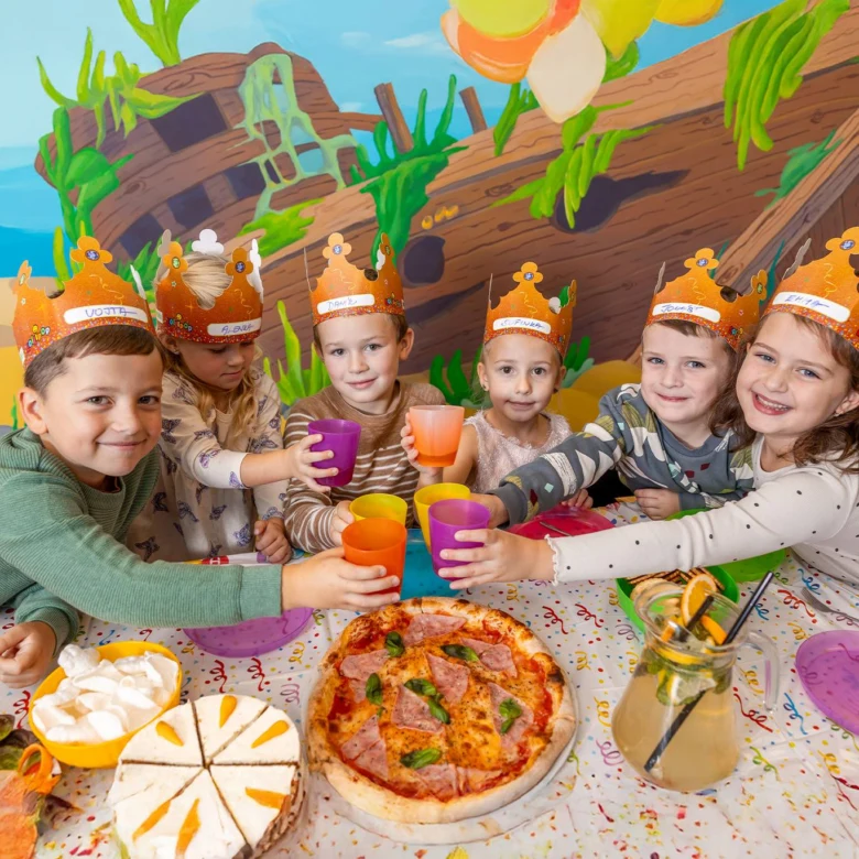 Děti s korunkami se radují ze svátku narozenin s pizzou.