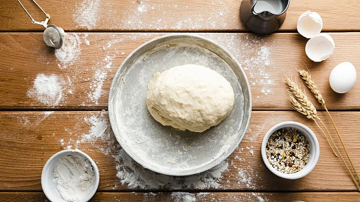 Kynuté těsto na pizzu s moukou a vejci v kuchyňské scéne.