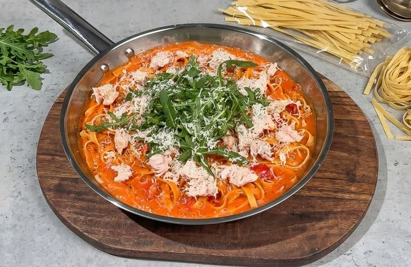 Pasta s rybami v omáčce na dřevěném podnosu.